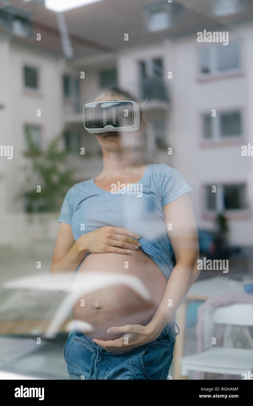 Schwangere Frau mit VR-Brille hinter Fensterglas Stockfoto