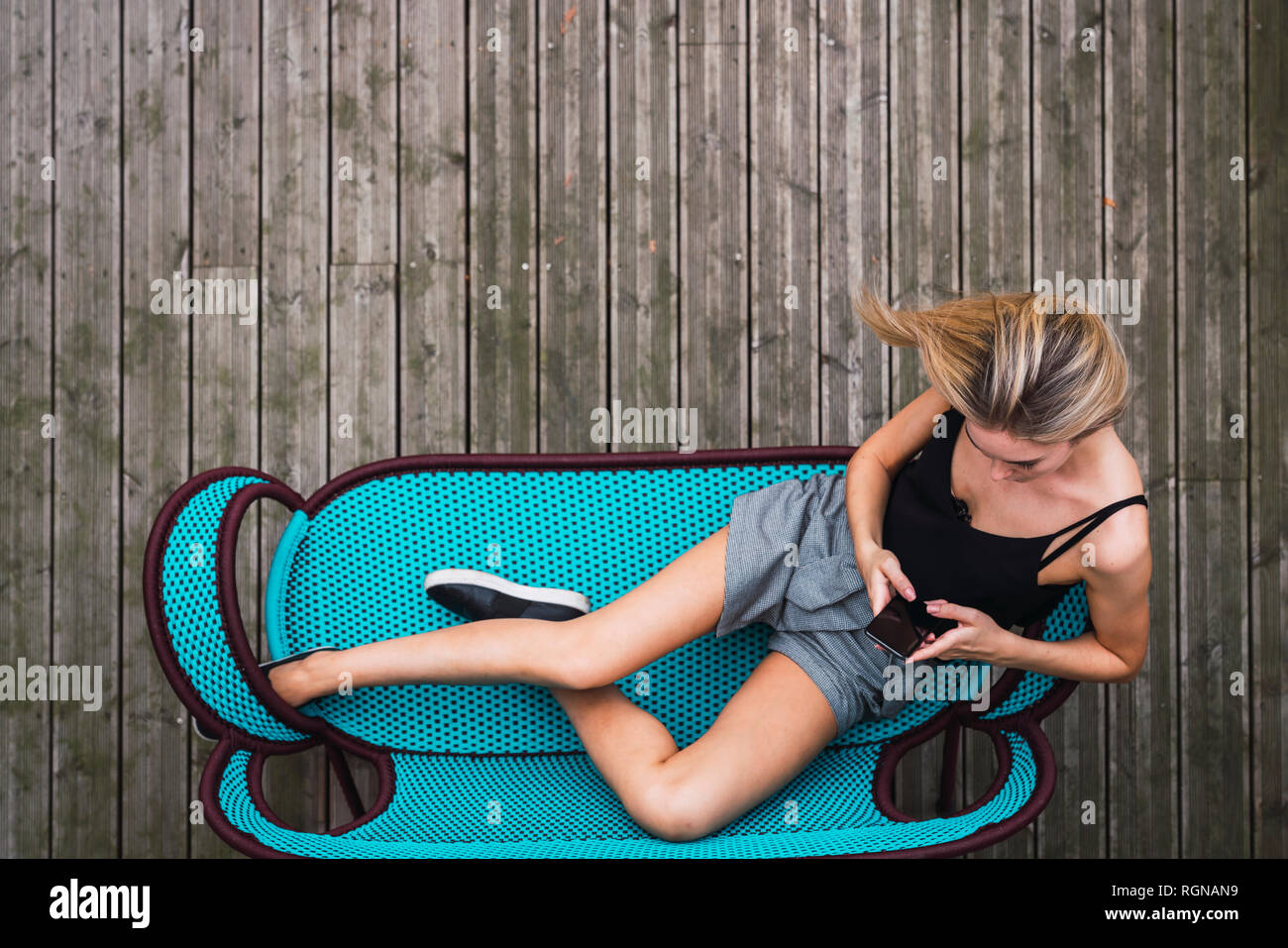 Junge Frau sitzt auf Türkis Tisch auf der Terrasse mit Smartphone, Ansicht von oben Stockfoto