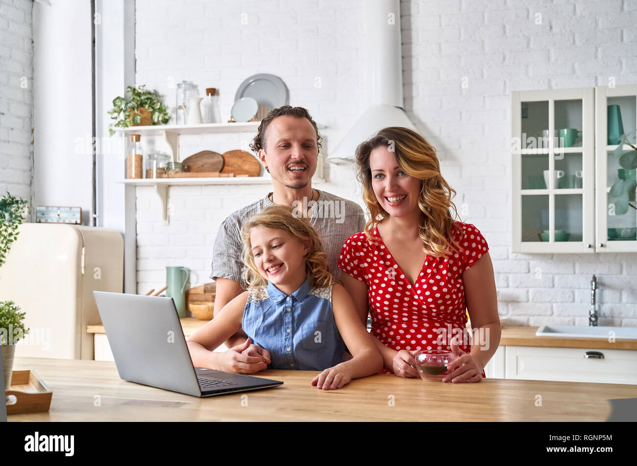 Glückliche Familie mit Laptop am Tisch in der Küche. Tochter, Mutter und Vater zusammen. Stockfoto