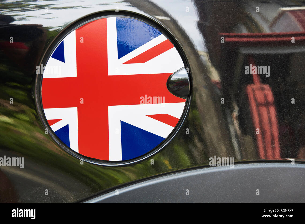 Nahaufnahme eines Runden tanken Kappe mit einer Gestaltung der nationalen Flagge von Großbritannien, durch schwarze glänzende auto Lack spiegelt die Umgebung umgeben Stockfoto