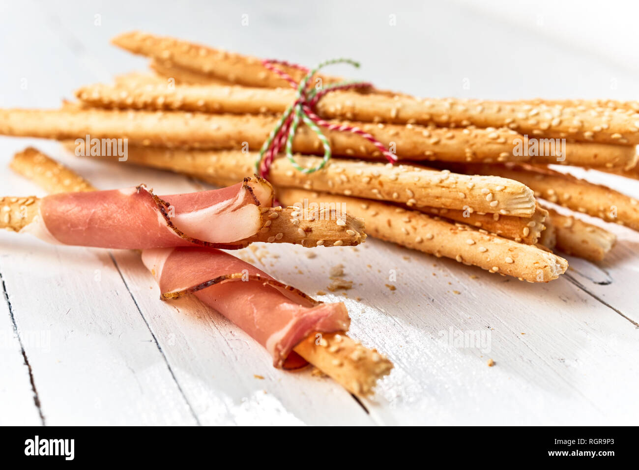 Frisch gebackene italienische grissini Brot Sticks in Schinken auf einem high key Holz Hintergrund gewickelt. Stockfoto
