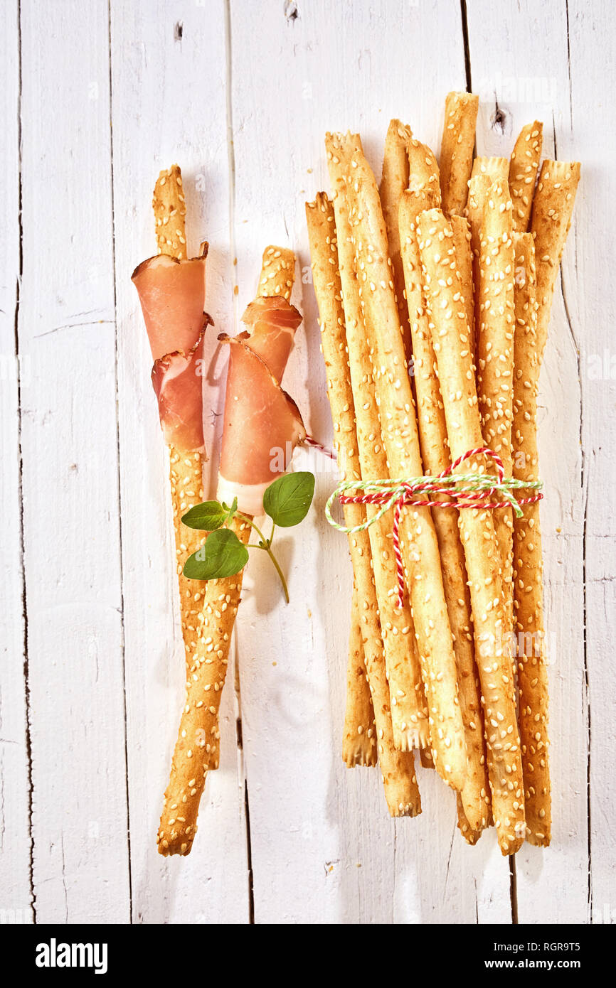 Knusprig gebackene italienische grissini Brot Sticks in Schinken gewickelt und mit frischen Kräutern auf einem high key Holz Hintergrund garniert. Stockfoto