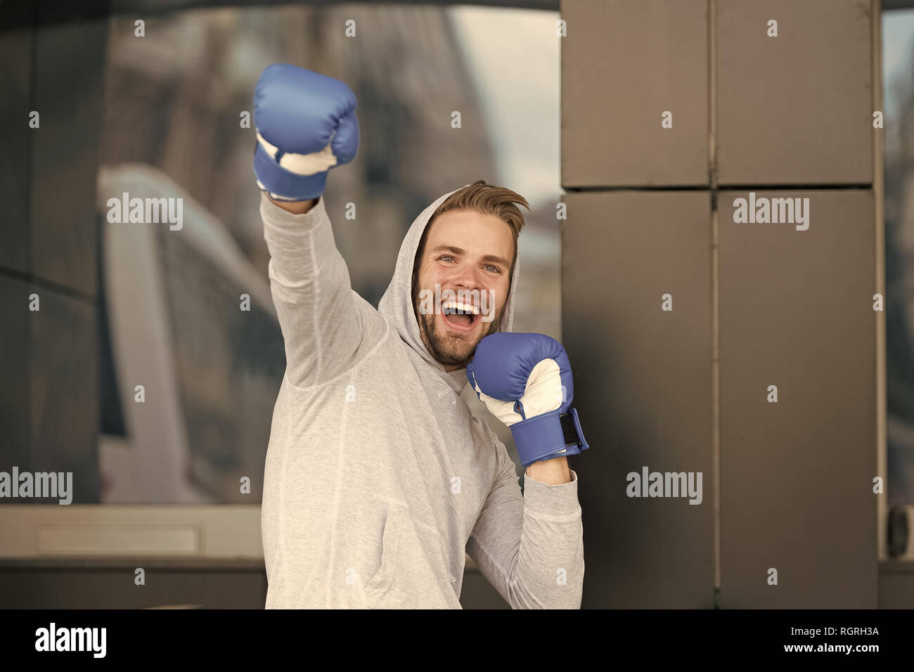 Sieger nimmt sie alle. Mann auf lächelnde Gesicht mit Boxhandschuhen als Sieger posiert, im städtischen Hintergrund. Sportler feiert den Sieg. Erfolg Konzept. Mann motiviert ehrgeizige mag gewinnen und Erfolg. Stockfoto