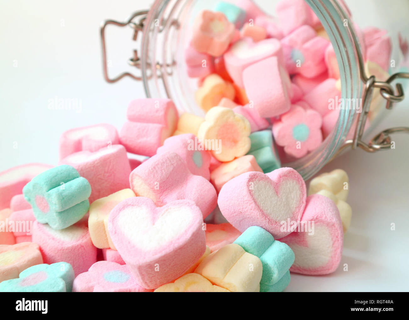 Haufen von Pastelltönen in Herzform und mit Blumen geformte Marshmallow Süßigkeiten verteilt aus Glas auf weißer Tisch, Valentine, Konzept Stockfoto