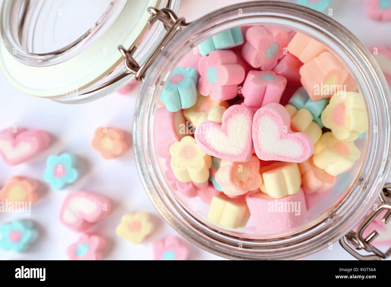 Ein Paar rosa Herzen auf dem Stapel von Pastell Blume geformte Marshmallow Bonbons im Glas mit einigen verstreut auf dem Tisch, Valentine, Konzept Stockfoto