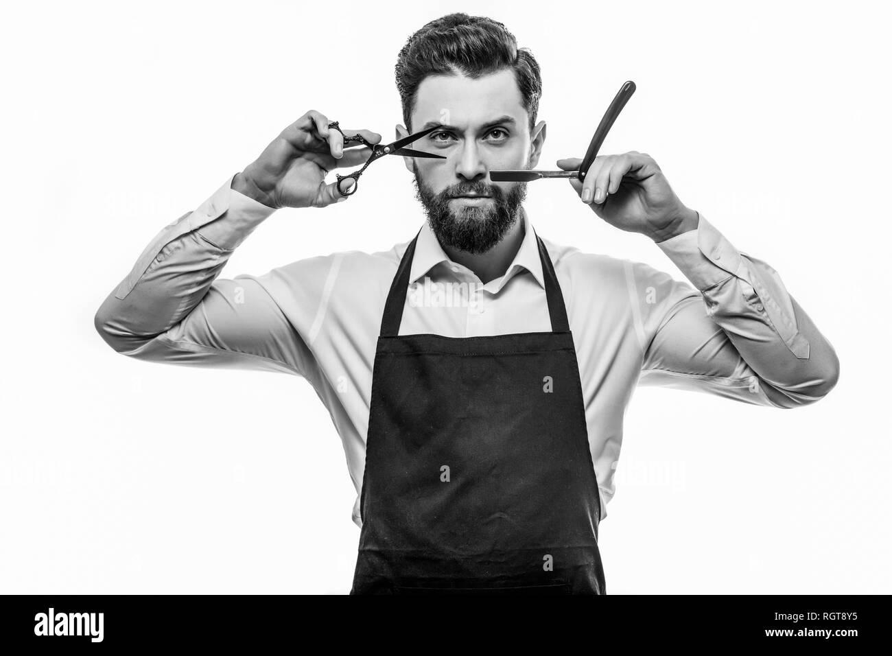 Portrait von Heiter fröhlichen Friseur mit Stoppeln in Shirt, Scheren, Werkzeuge, Ausrüstungen in die Hände an der Kamera auf grauem Hintergrund suchen Stockfoto