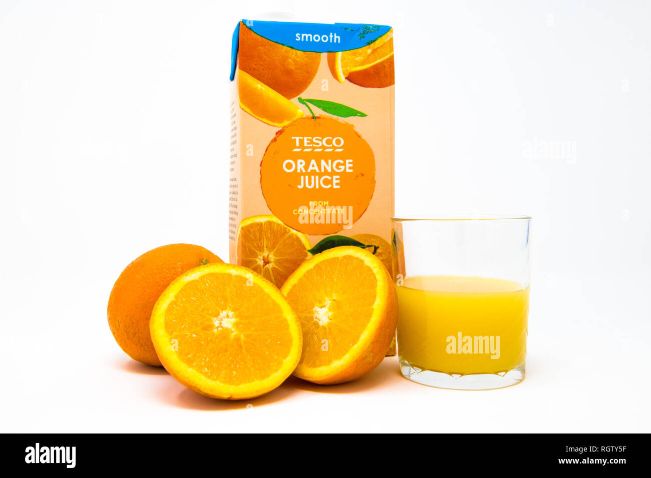 Karton von Tesco's Orangensaft Konzentrat mit frisch geschnittenen Orangen und Glas halb voll. Stockfoto