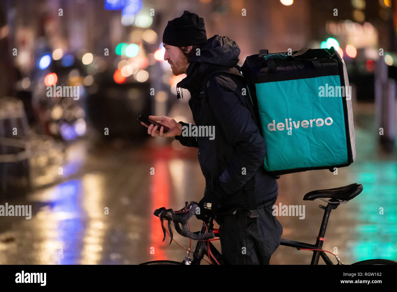 Eine Deliveroo Lieferung Reiter steht, während Sie ein Telefongespräch auf einem Fahrrad in der Queen Street in Cardiff, Wales, UK. Stockfoto