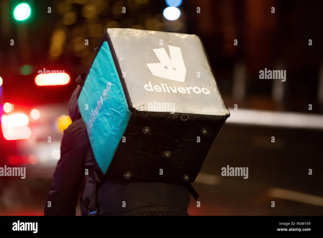 Eine Deliveroo Reiter reitet ein Bike mit einem Deliveroo Beutel in der Nacht in Cardiff, Wales, UK. Stockfoto