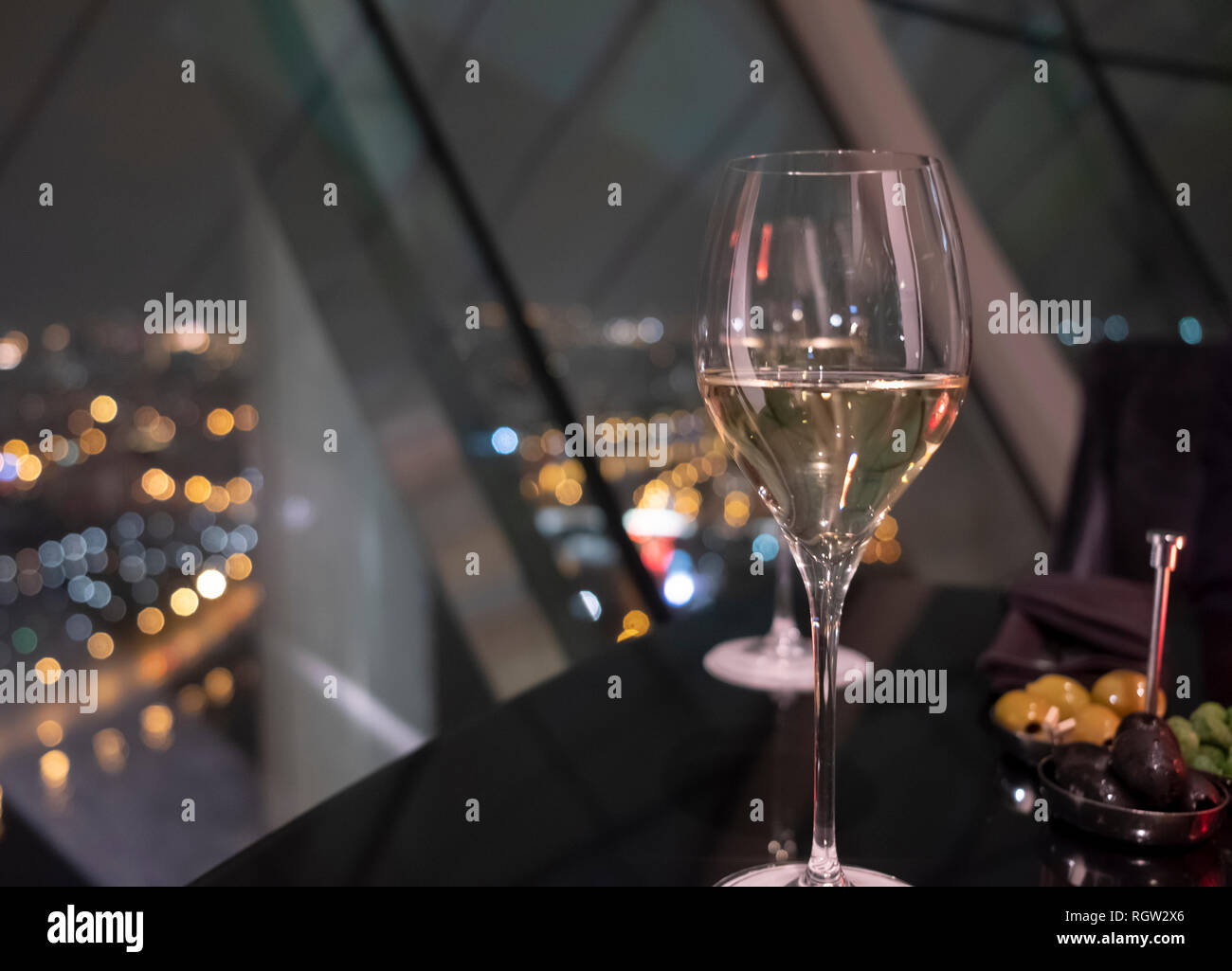 Glas Weißwein auf einem Schwarzen Tisch im Restaurant. Nacht Lichter der Stadt bokeh durch Panoramafenster im Hintergrund. Erholung im Luxushotel Stockfoto