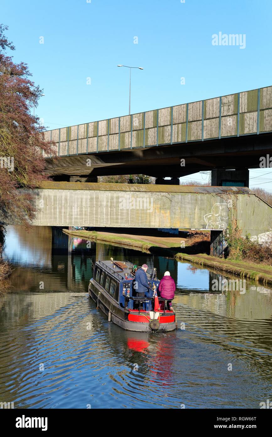 Ein schmales Boot auf der Kreuzung der Wey Navigation und der Basingstoke Canal an New Haw, mit erhöhten Abschnitt der Autobahn M25, Surrey, England Stockfoto