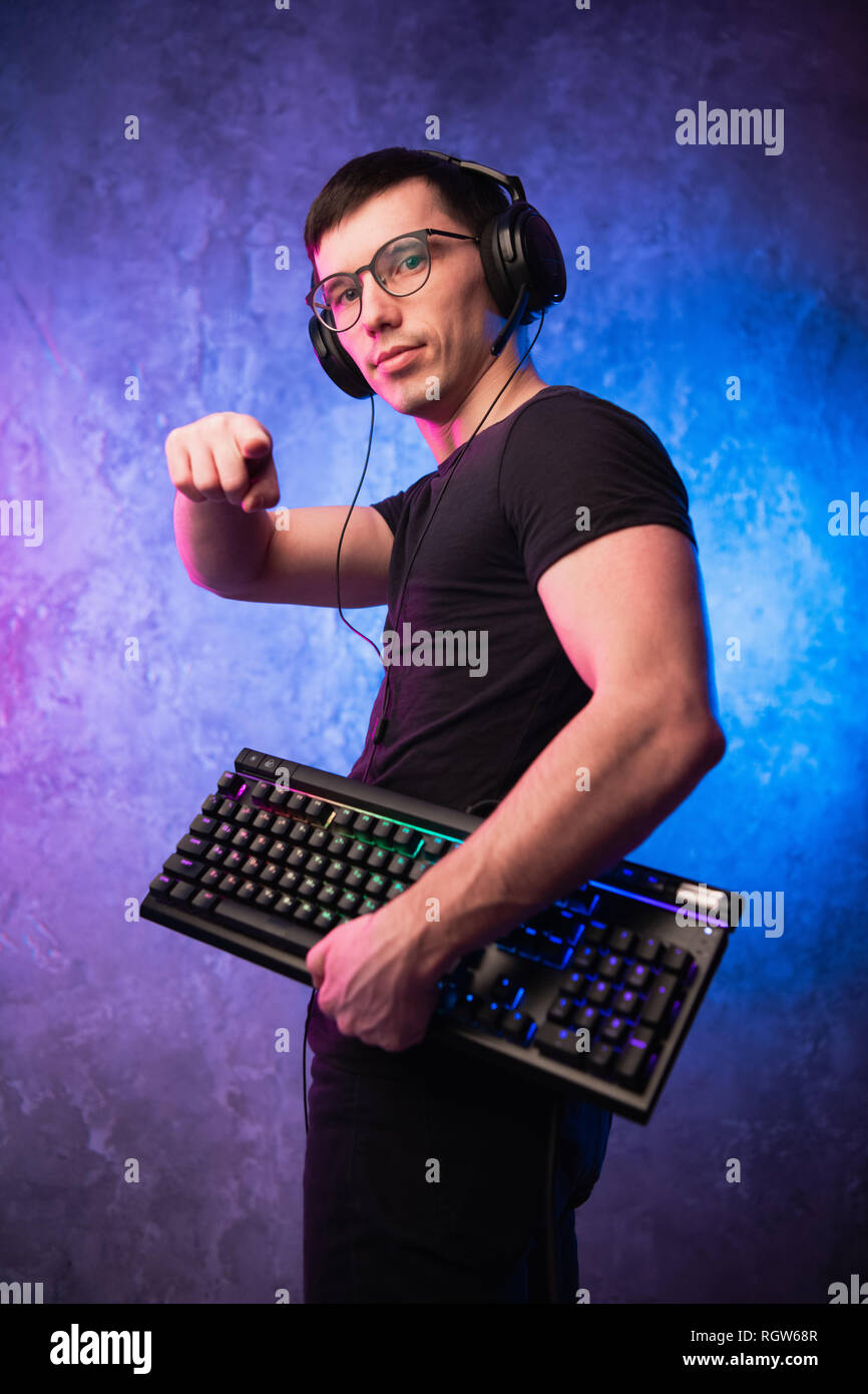 Junge schöne Gamer das Headset mit Mikrofon, halten Sie eine Tastatur und einen Zeigefinger an der Kamera auf Neon farbigen Hintergrund Stockfoto