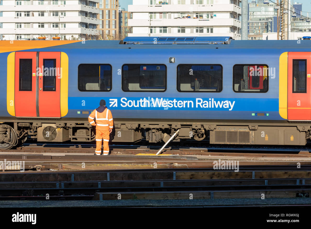 Clapham Junction, UK, 30. Januar 2019; South Western Railway Mitarbeiter in Orange Hi Sichtbarkeit Sicherheit Kleidung steht Vor vorbeifahrenden Zug Stockfoto