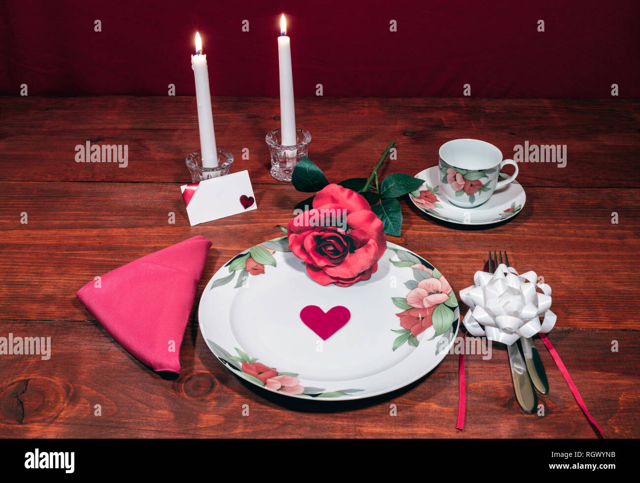 Florales Muster, feines Porzellan Geschirr mit passenden Teller, Tasse und Untertasse. Rosa Rosa, Pink serviette, Besteck, weiße Kerzen und Karte. Stockfoto