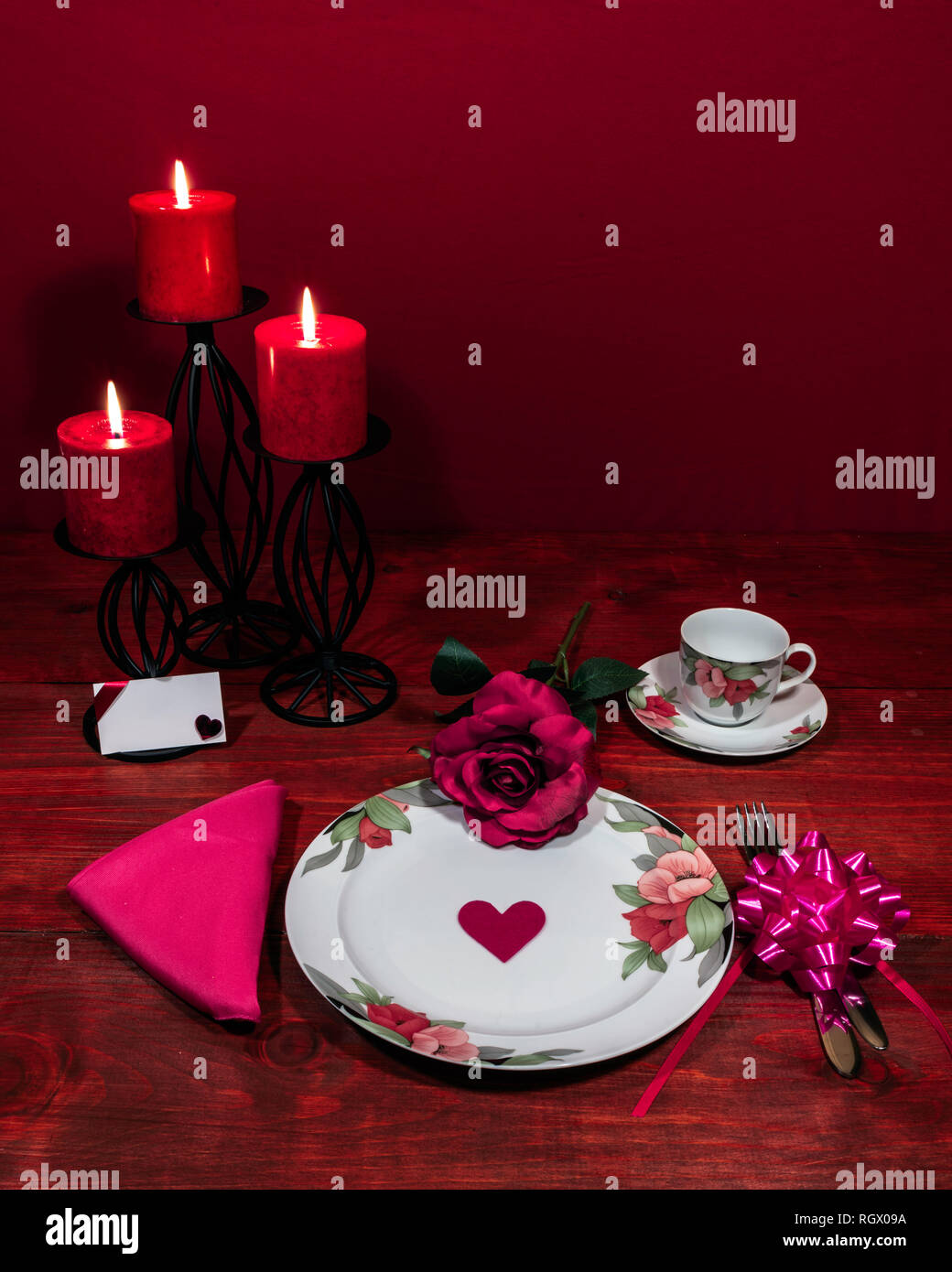 Florales Muster, feines Porzellan Geschirr mit passenden Teller, Tasse und Untertasse. Rosa Rosa, Pink serviette, Besteck, rote Kerzen und Karte. Stockfoto
