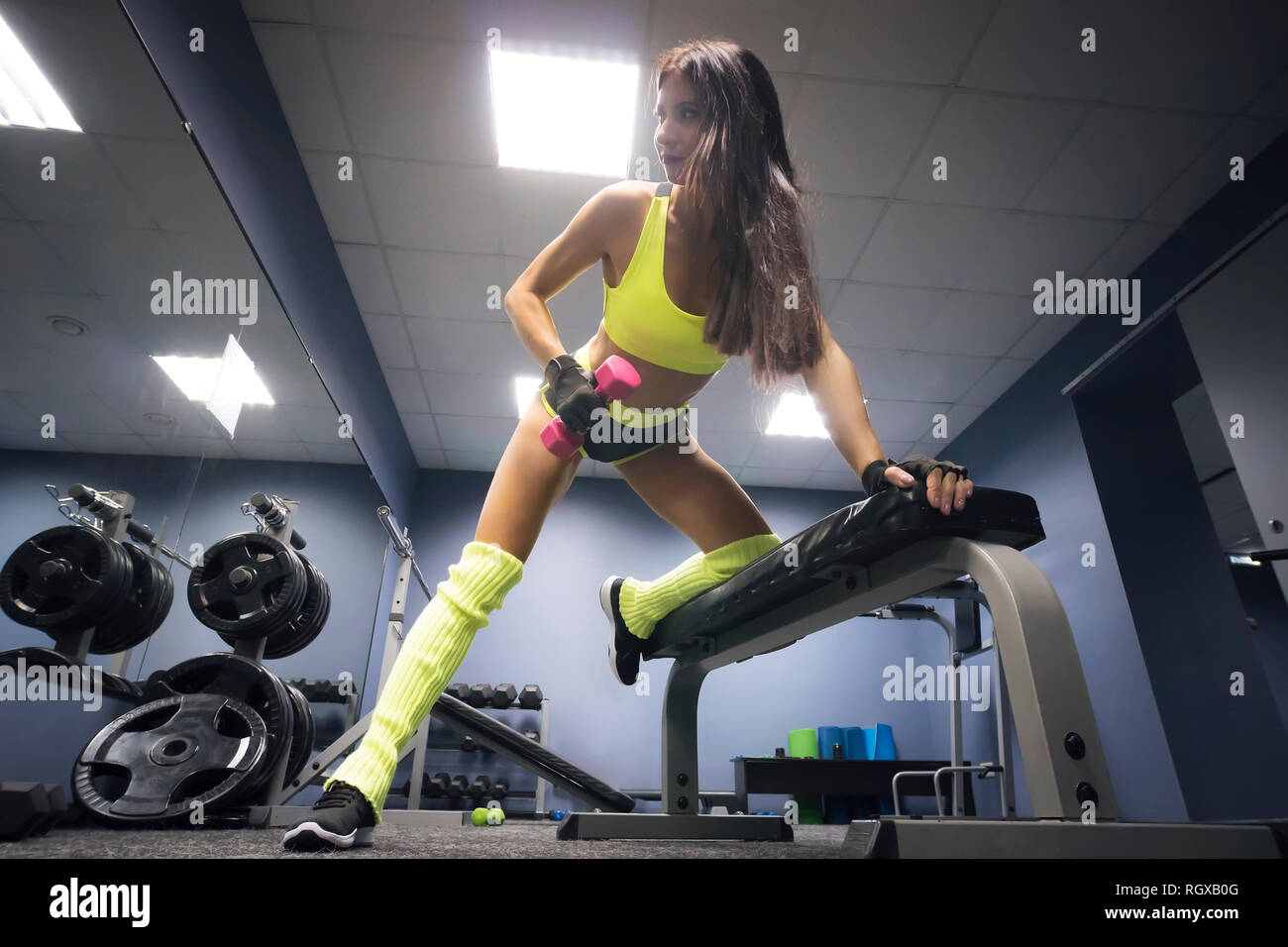 In voller Länge Porträt der jungen Schlank fitness Frau heben rosa Hanteln in der Turnhalle. Modell mit Fitnessgeräten in leeren Health Club Zimmer posieren. Ath Stockfoto