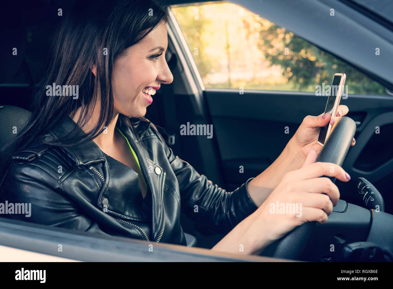Glücklich lächelnde Frau mit Ihrem Smart Phone in einem Auto sitzen. Weibliche Treiber Lachen lesen Nachricht und Chatten in Mobile. Mädchen schaut sie Cel Stockfoto