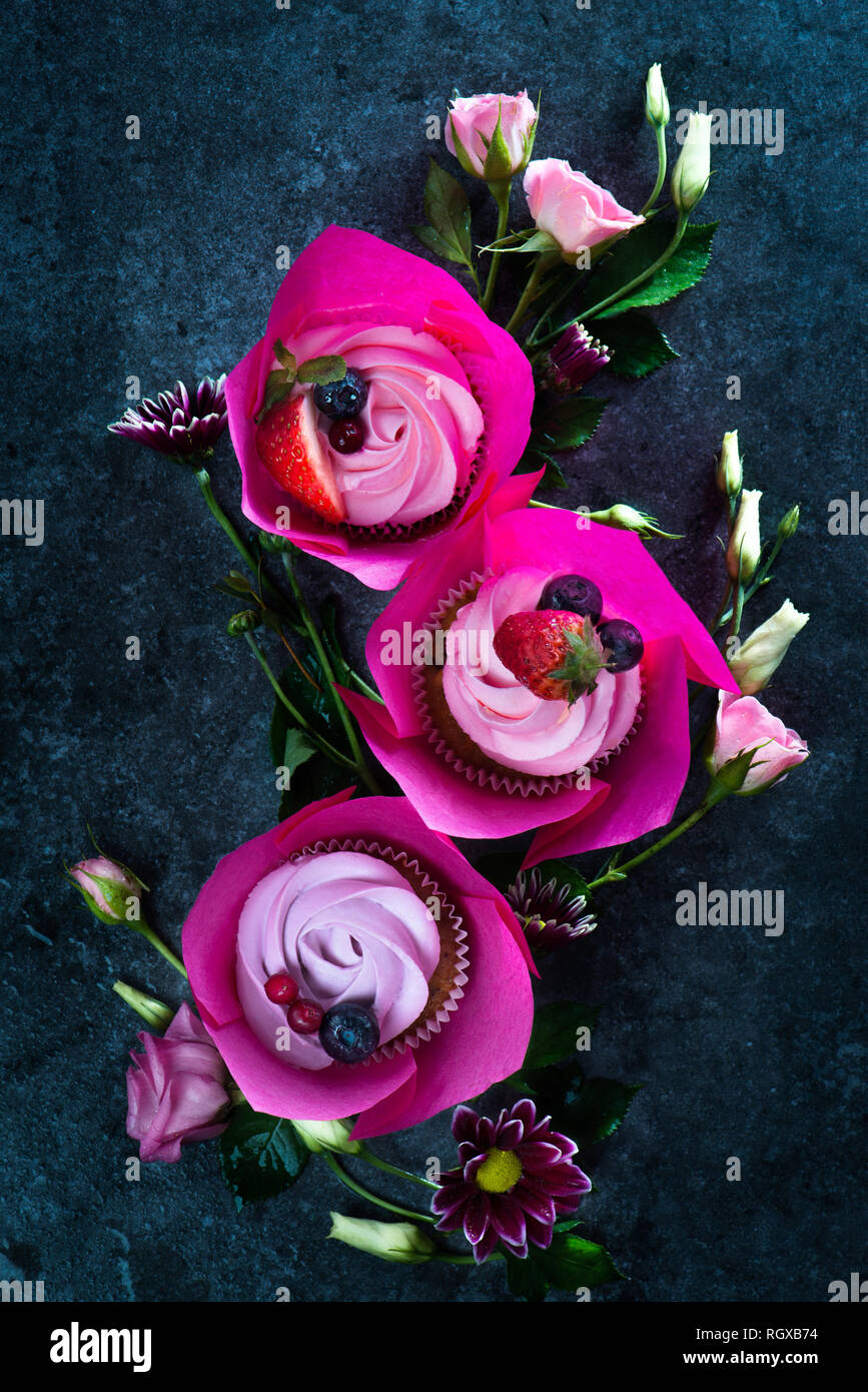 Cupcakes mit rosa umhüllt und rosa Blüten auf einem dunklen Hintergrund. Feder Dessert für drei mit Kopie Raum Stockfoto