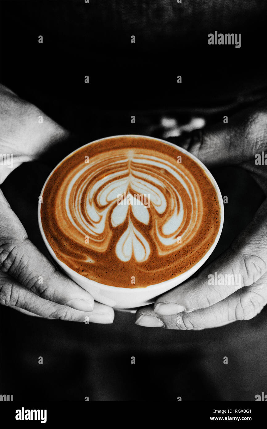 Eine Tasse Kaffee mit einem Herzen latte Schaum Kunst auf der Oberseite, helf von männlichen Händen, in Schwarz und Weiß, Monochrom. Stockfoto