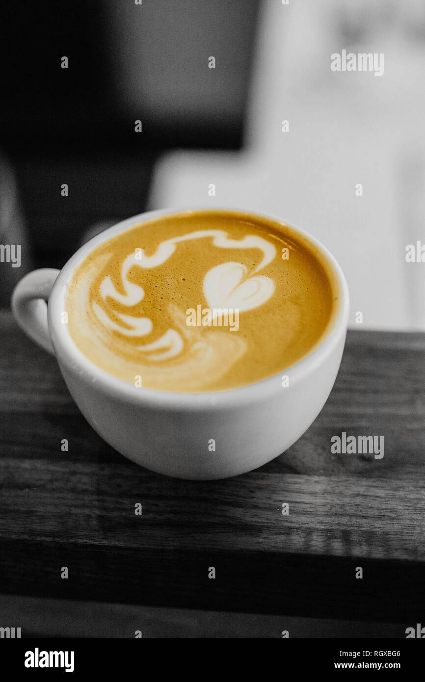 Eine weiße Tasse Kaffee mit einem Herzen latte Schaum Kunst auf, sitzen auf einem Tisch, in Schwarz und Weiß, Monochrom. Stockfoto