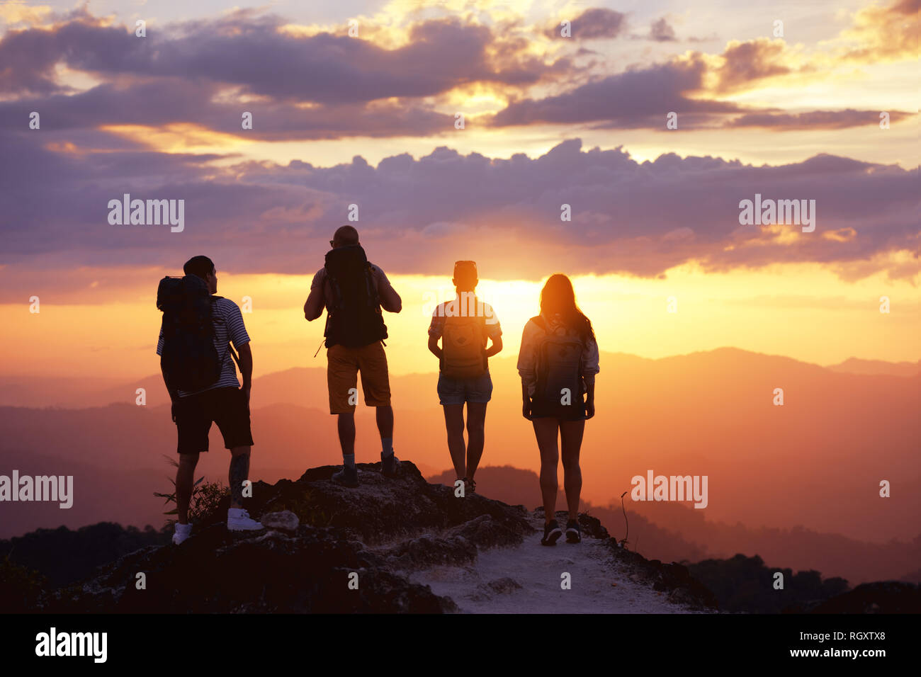 Gruppe von vier Touristen oder Freunde steht auf einem Berg und schaut bei Sonnenuntergang. Völker Travel Concept Stockfoto