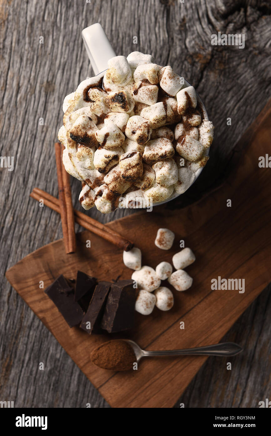 Overhead shot von einer Tasse heißem Kakao mit gerösteten Marshmallows neben ein Schneidebrett mit Schokolade Chunks und Zimtstangen. Vertikales Format-Sha Stockfoto