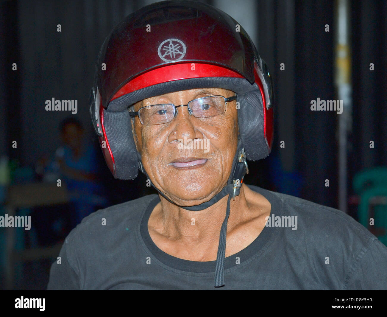 Alte indonesische Mann mit Brille trägt ein modernes, rotes Motorrad Helm. Stockfoto