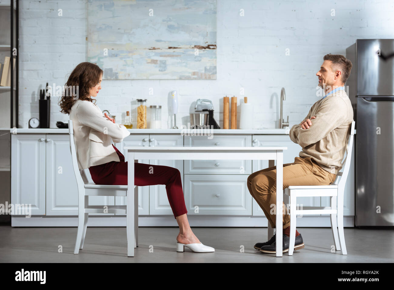 Unzufrieden Paar sich einander beim Sitzen mit am Tisch in der Küche gekreuzt Stockfoto