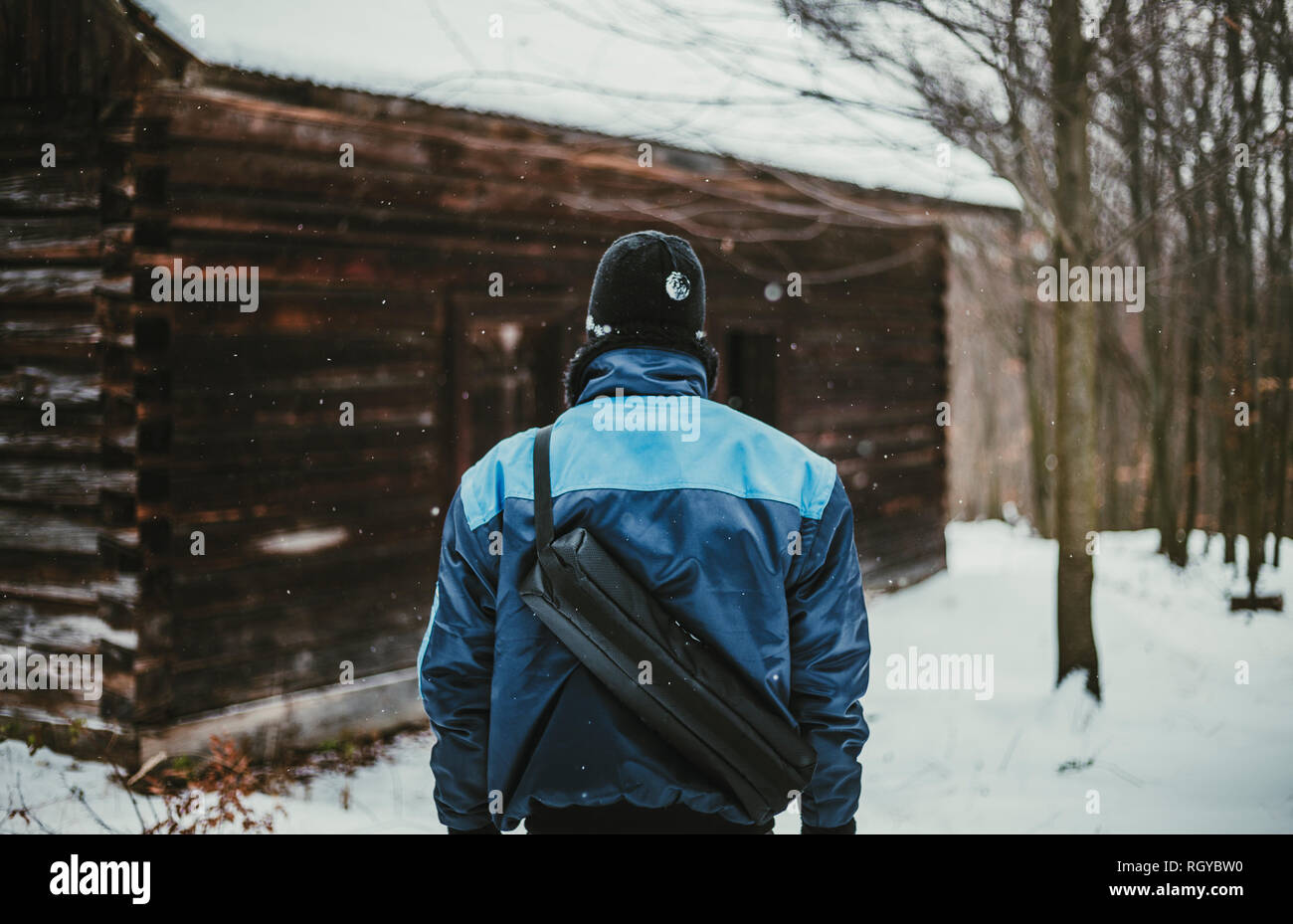 Foto der Abenteurer (Wanderer) im verschneiten Wald vor der verlassenen Hütte (Blick von seinem Rücken). Wanderer Mann in der blauen Jacke steht in den Bergen Stockfoto