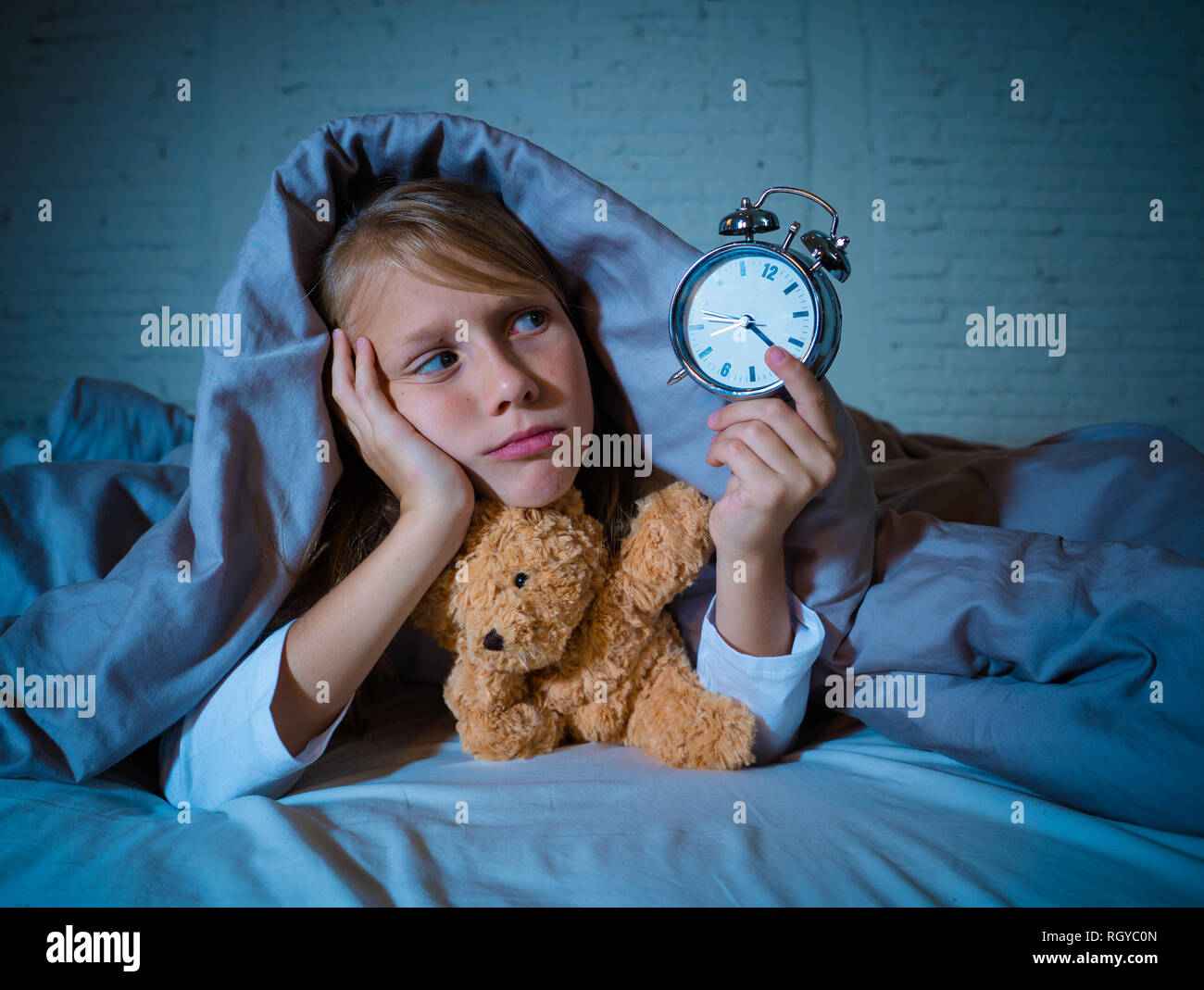 Cute schlaflose kleines Mädchen im Bett liegend zeigt Wecker müde in das Schlafen Probleme schlafend nachts aufhalten oder wachen zu früh in Chil Stockfoto