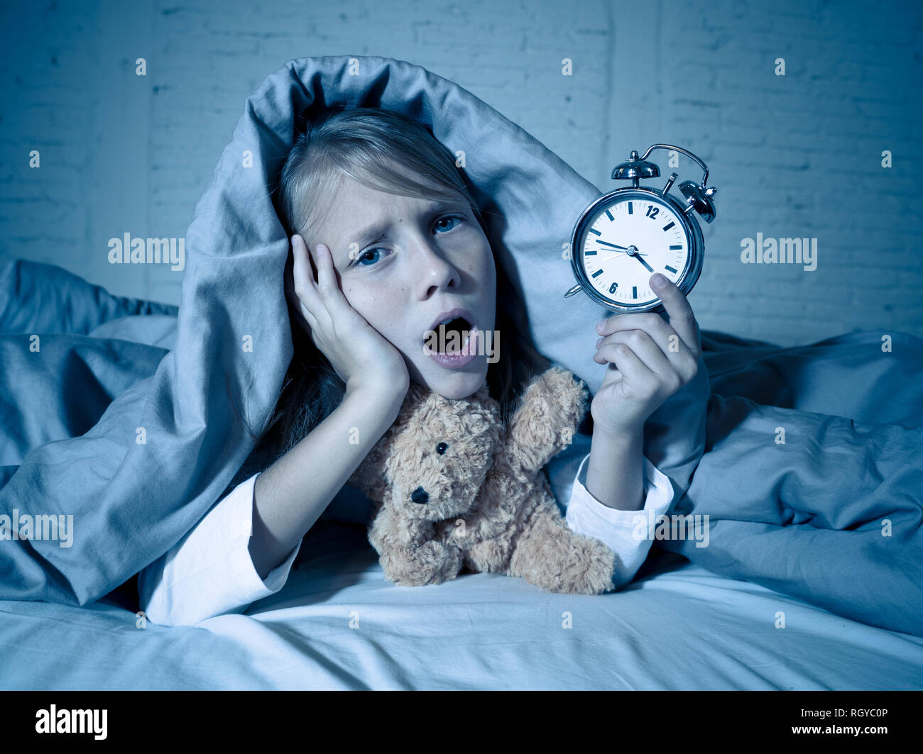 Cute schlaflose kleines Mädchen im Bett liegend zeigt Wecker müde in das Schlafen Probleme schlafend nachts aufhalten oder wachen zu früh in Chil Stockfoto
