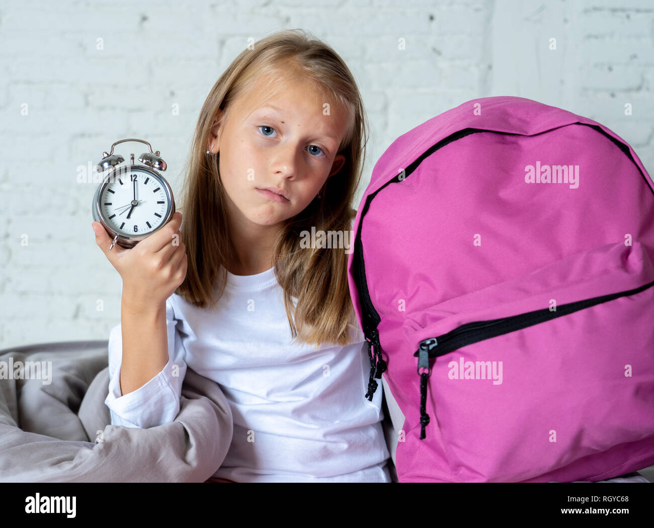 Schöne blonde Mädchen traurig Schlaflose und verärgert zeigt Wecker Zeit, machen Sie sich bereit für die Schule in Schwierigkeiten Aufwachen am Morgen Childre Stockfoto