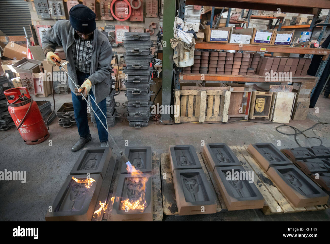 Rupert Francis legt Feuer in den Sand wirft, wie sie bereit sind, für das Metall in der Hand gegossen zu werden - aus Gießen der Britischen Akademie für Film und Fernsehen Awards (BAFTA) Masken in einer Gießerei in West Drayton, London vor der Preisverleihung am 10. Februar. Stockfoto