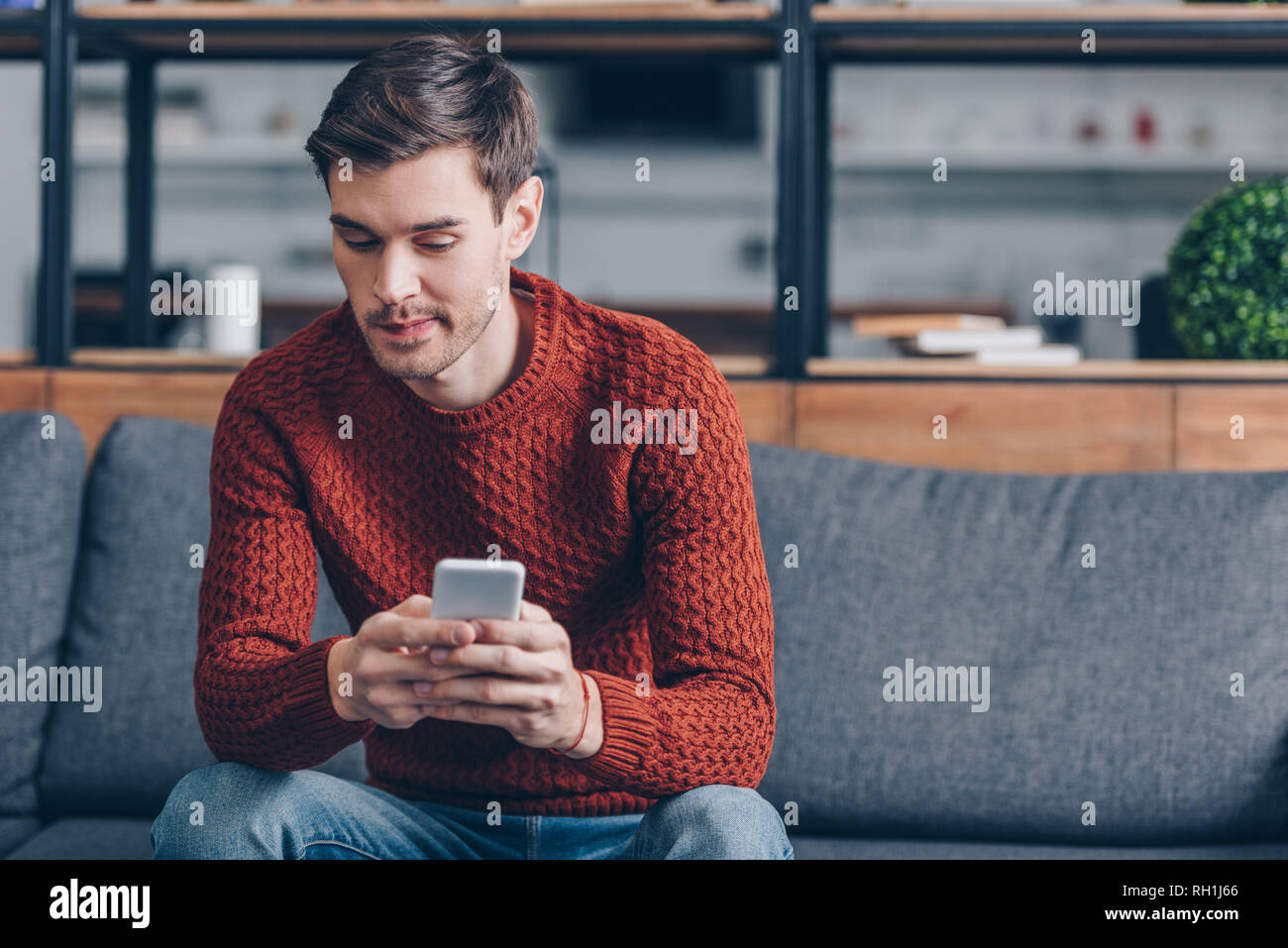 Nachdenklicher junger Mann sitzt auf einem Sofa und sie ihr Smartphone zu Hause Stockfoto