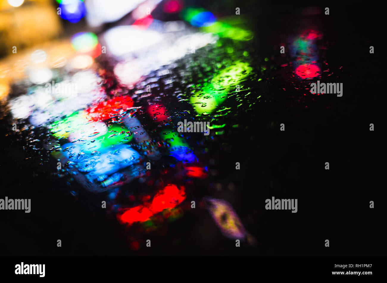 Bunte Reflexionen und Regentropfen auf nassen schwarzen Auto Haube. Abstract Night city verschwommenen Hintergrund Stockfoto