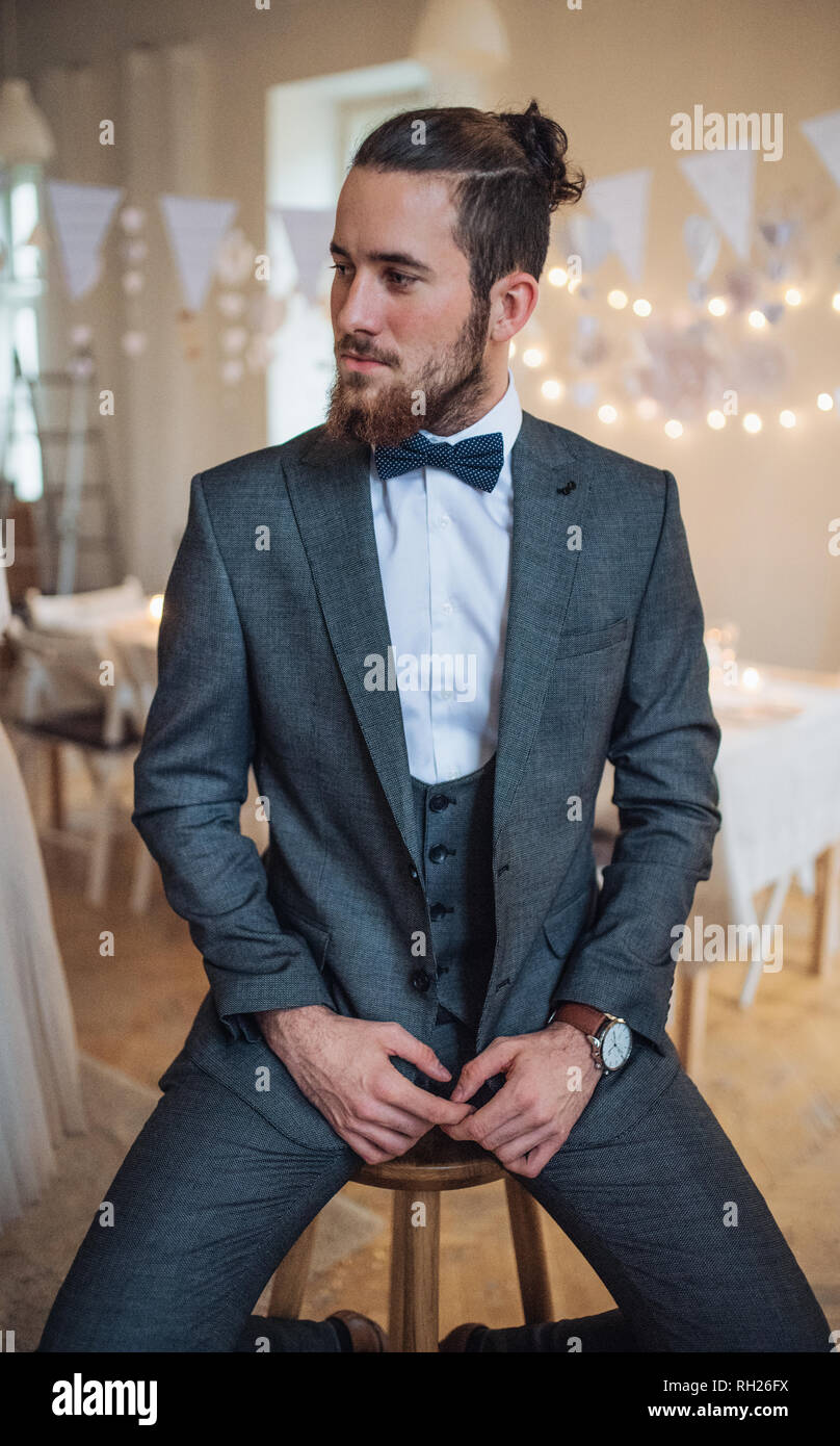 Ein schöner Hipster junger Mann mit Anzug saß auf einem Stuhl an einem Indoor Party, weg schauen. Stockfoto