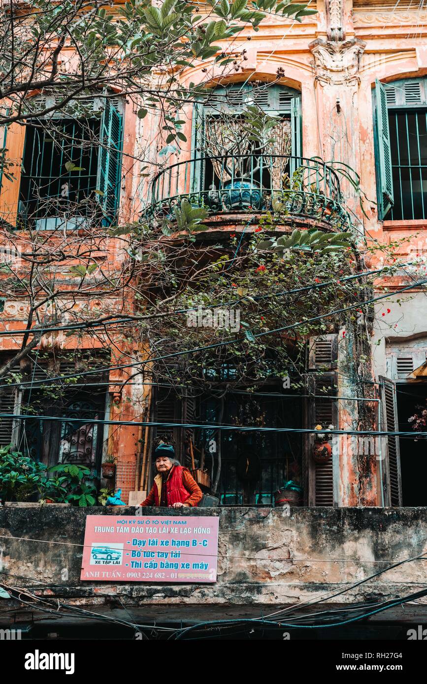 Hanoi, Vietnam, 12.20.18: Das Leben auf der Straße in Hanoi. Alte Dame auf einem Balkon in einem alten Gebäude. Stockfoto