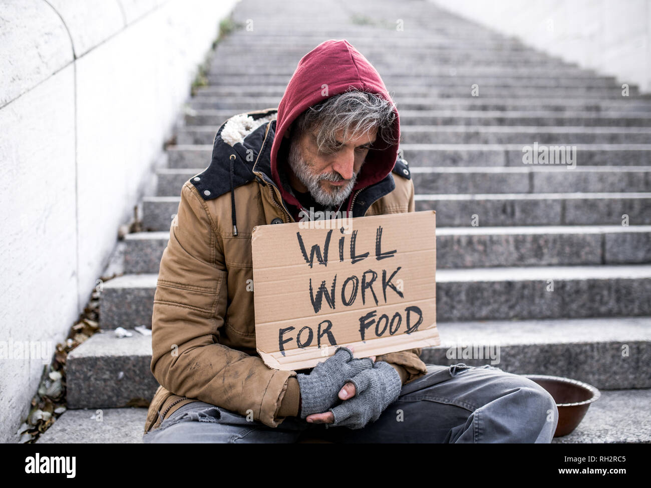 Eine obdachlose Bettler Mann sitzt auf der Treppe im Freien in Stadt bitten um Geld Spende. Stockfoto