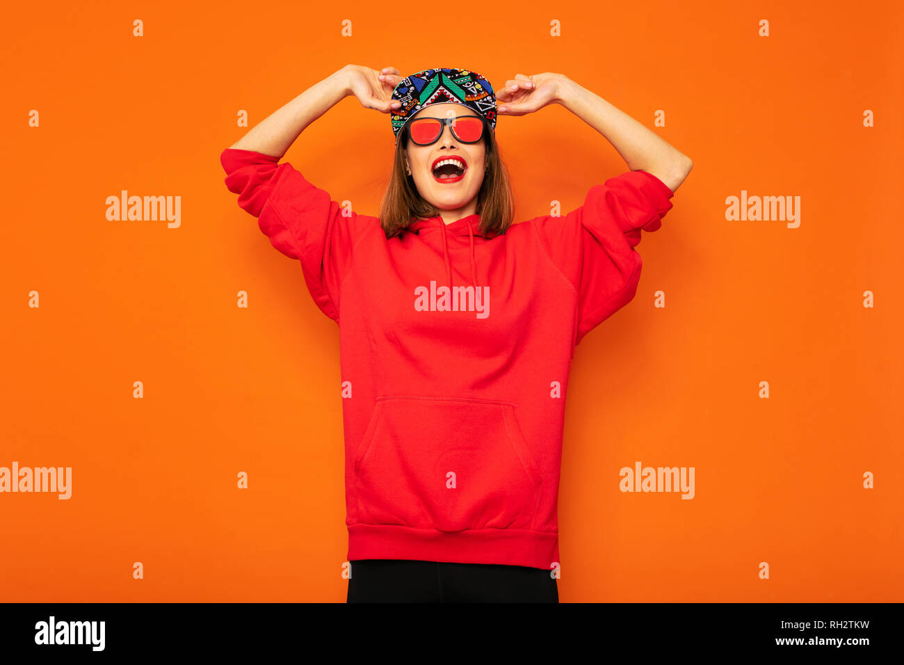 Junge und coole hipster Mädchen Spaß, mit bunten Hut und Sonnenbrille mit guten vibes zu Kamera posieren auf orange Hintergrund Stockfoto