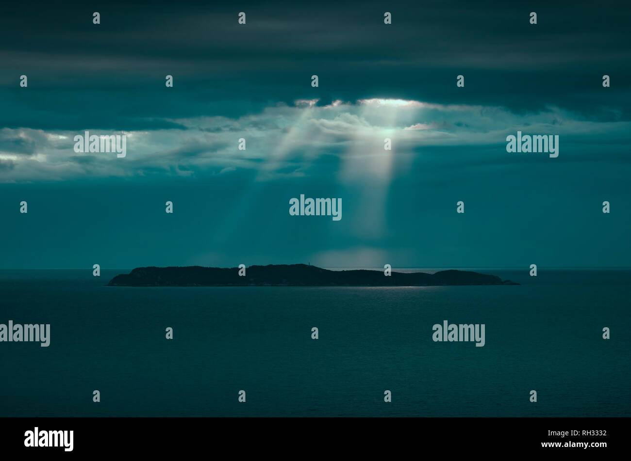 Kleine Insel mit einem Leuchtturm mitten im Meer bei Sonnenaufgang. Sonnenstrahlen durch die Wolken und das Berühren der Insel. Ilha de Gale-Bombi Stockfoto