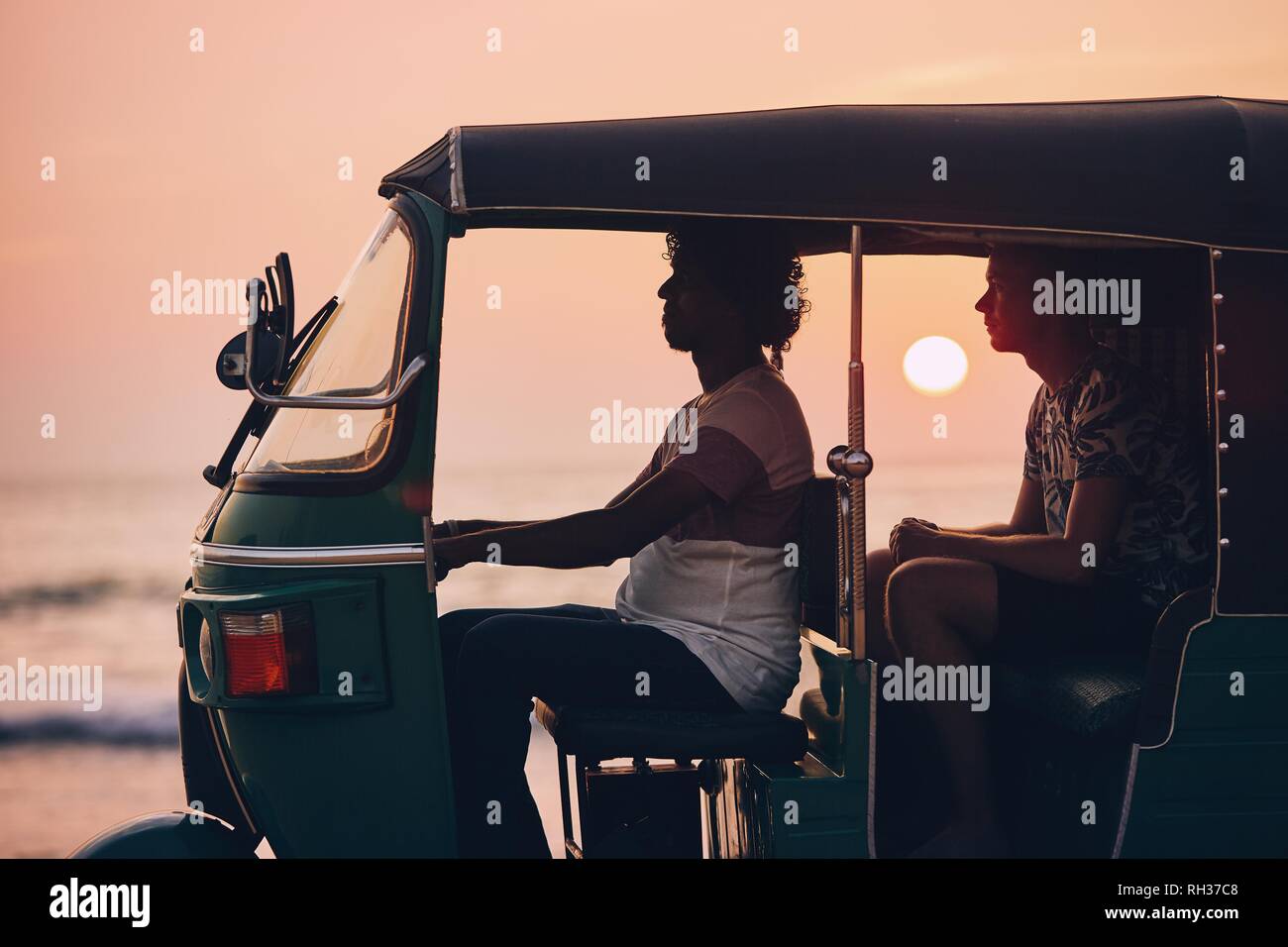 Fahrer und Beifahrer sind Reisen mit dem tuk tuk Taxi vor der See bei Sonnenuntergang in Sri Lanka. Stockfoto