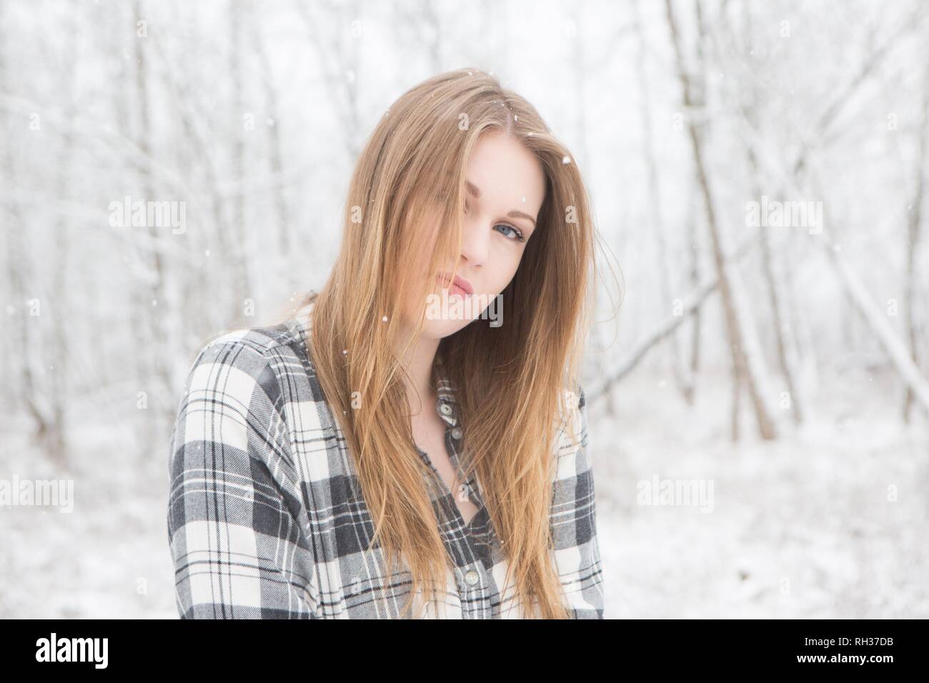 Junge Frau in Schwarz und Weiß Plaid Shirt stading in einem verschneiten Wald. Stockfoto