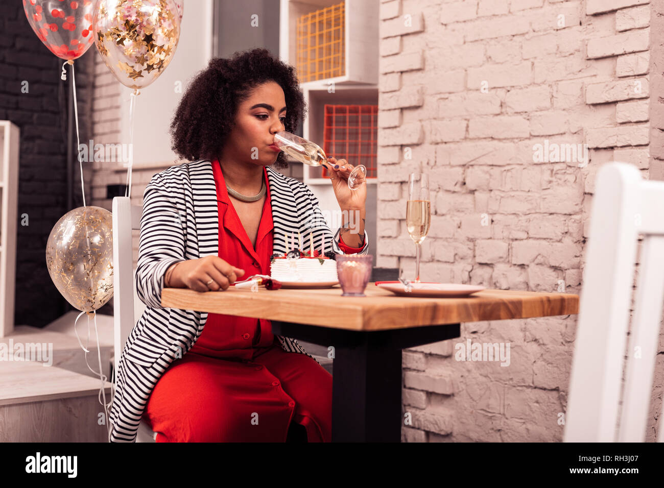 Angenehme afro-amerikanische Frau, die einen Schluck Champagner Stockfoto