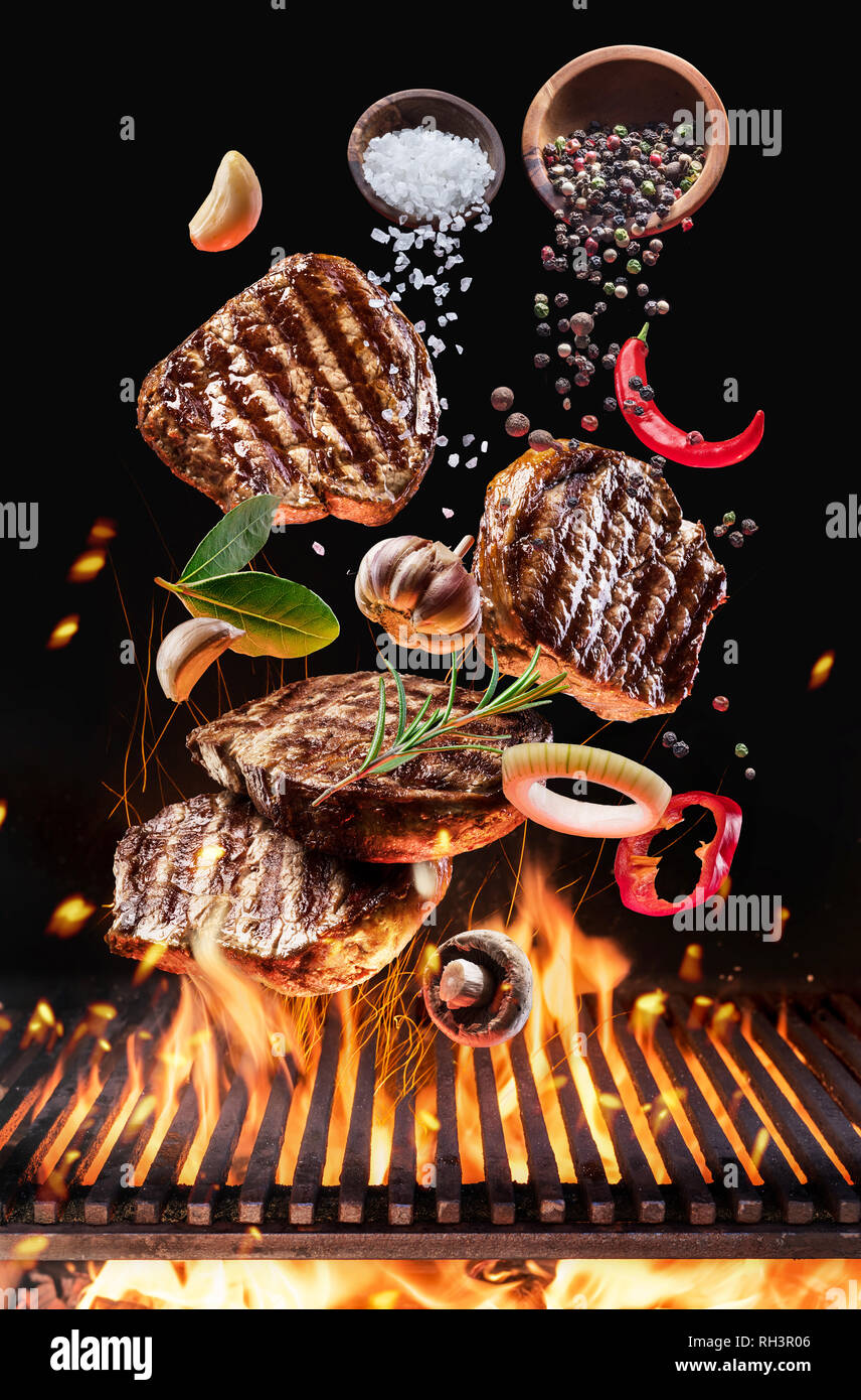 Gegrillte Rindersteaks mit Gemüse und Gewürze fliegen über den brennenden Grill Grill Feuer. Konzept der Flying Food. Stockfoto
