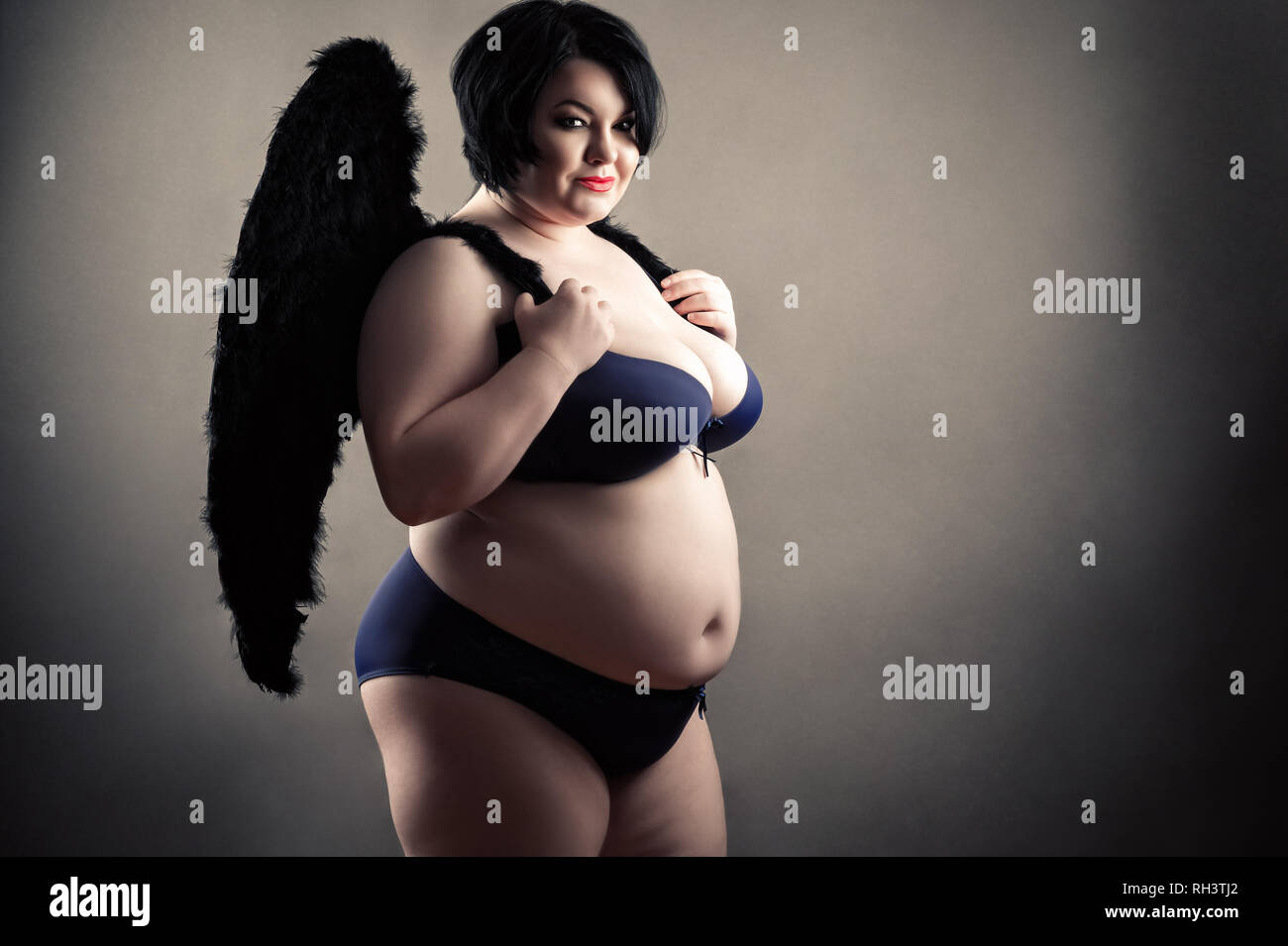 Charmante fette Frau in modischen Dessous mit schwarzen Flügeln Stockfotogr...