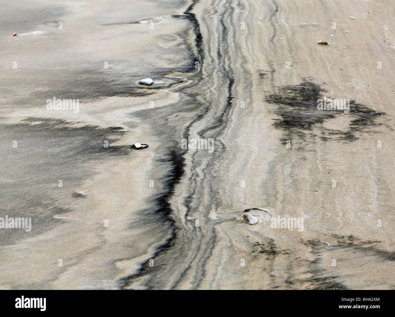 Schwarz und tan sand Muster Ursachen von Wellen entlang der Küste Stockfoto
