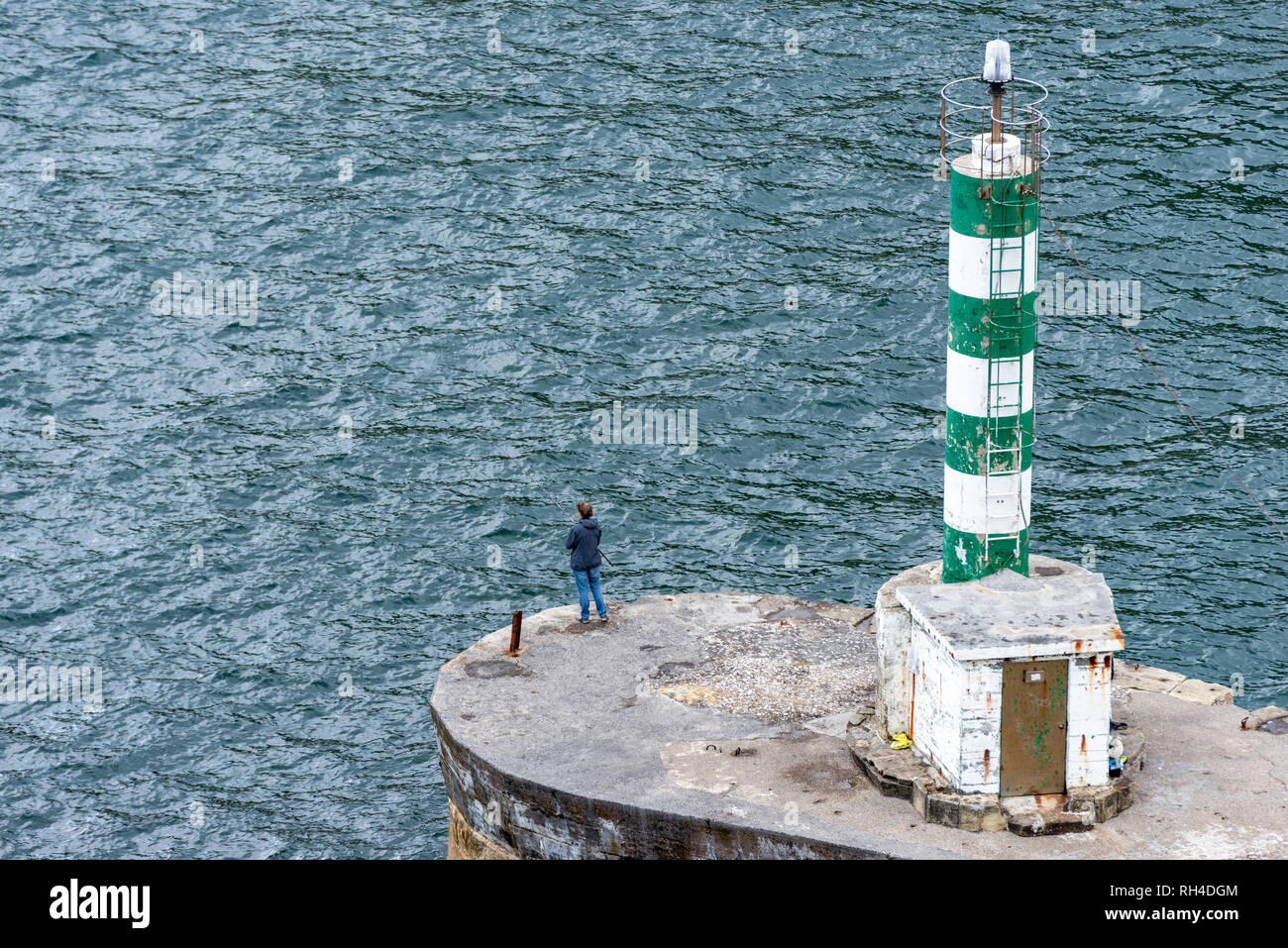 Einsame Fischer bei Grün weiß gestreift Leuchtfeuer am Meer Stockfoto