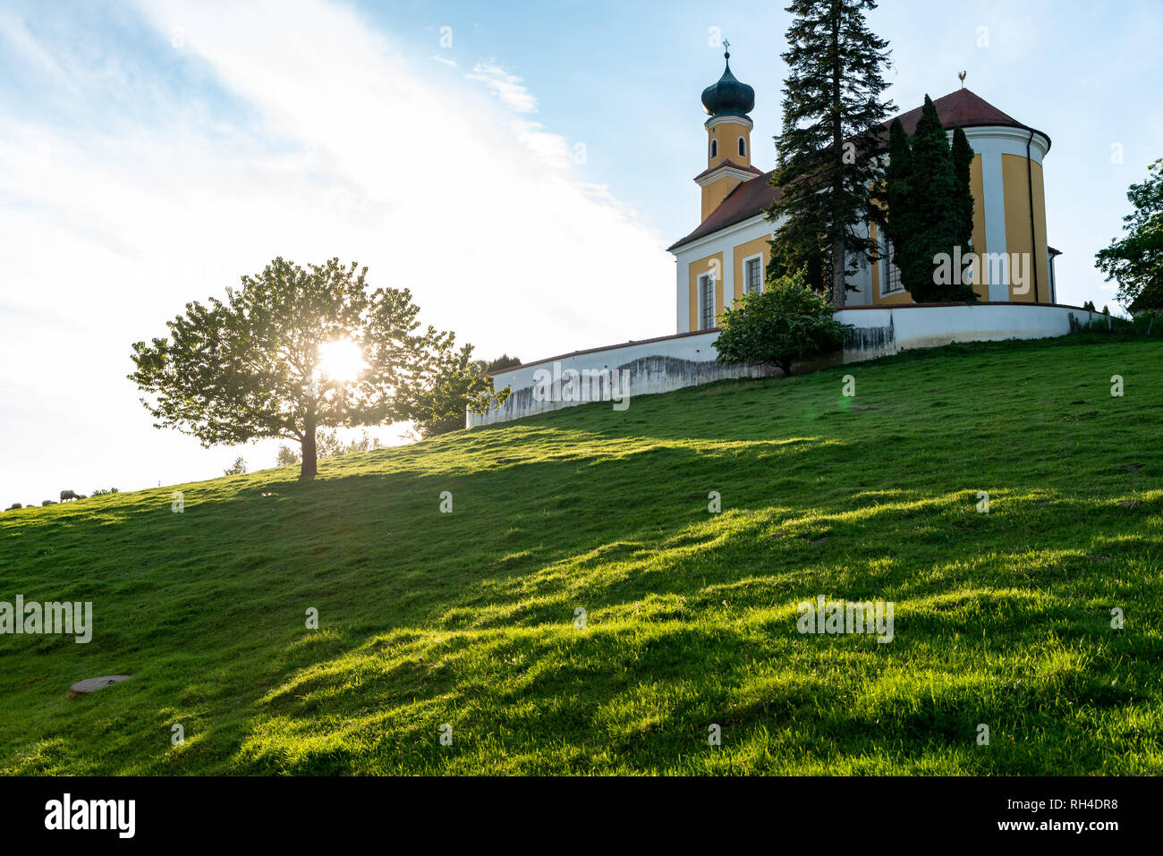 Bayerischen Kirche auf einem Hügel mit einem Outshined Baum von einem niedrigen Standpunkt aus gesehen Stockfoto