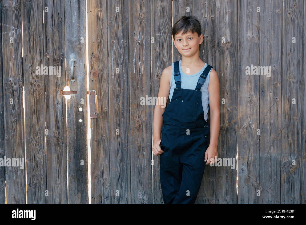 Portrait zuversichtlich Junge in Overalls an den hölzernen Zaun Stockfoto