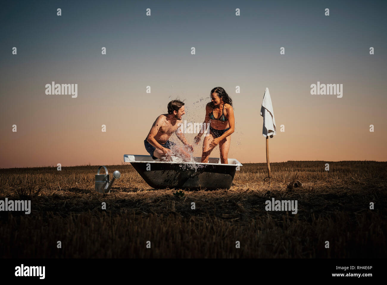 Verspieltes Paar, das in der Badewanne auf dem ländlichen Feld planscht Stockfoto